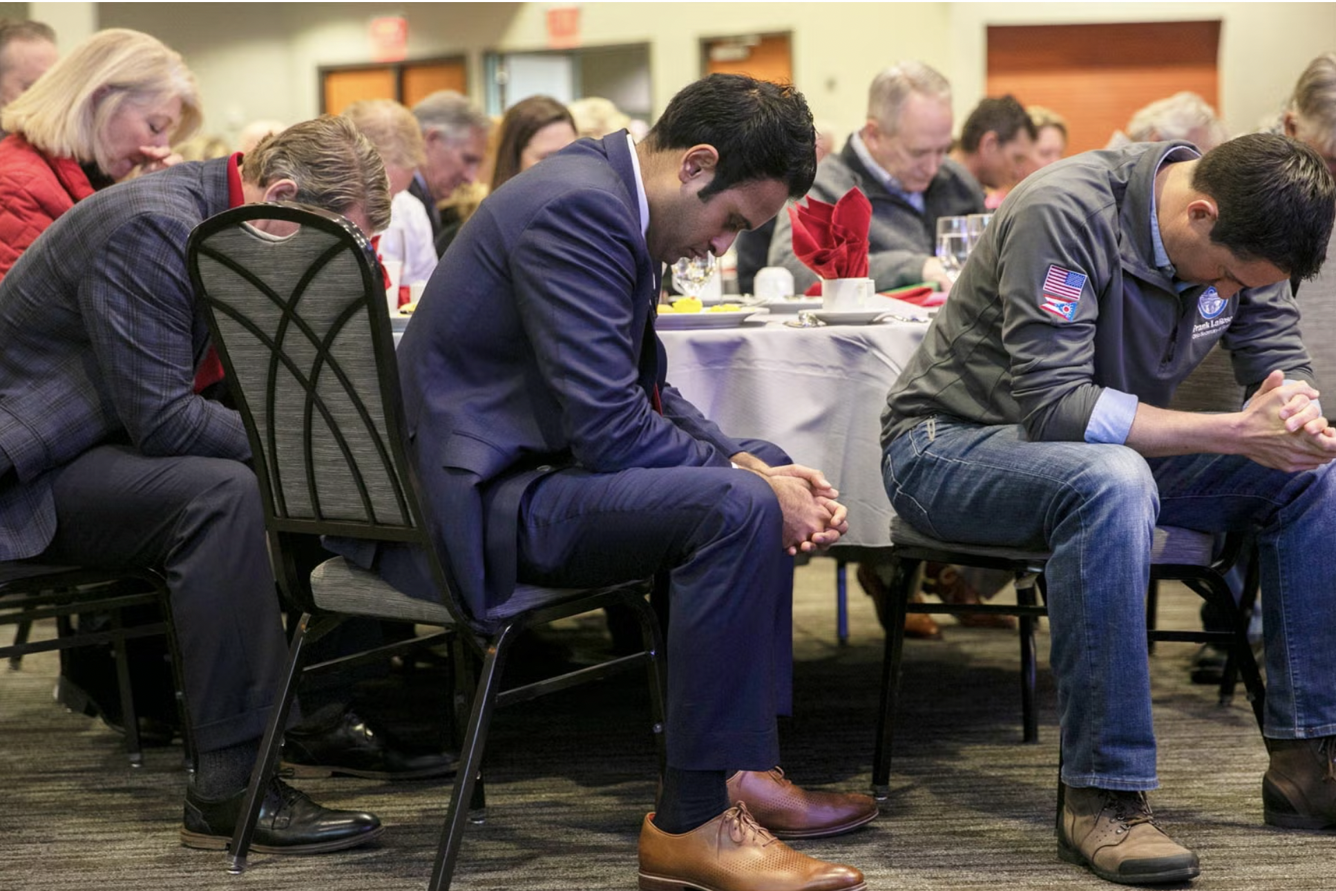 People seated at tables with their heads bowed in prayer