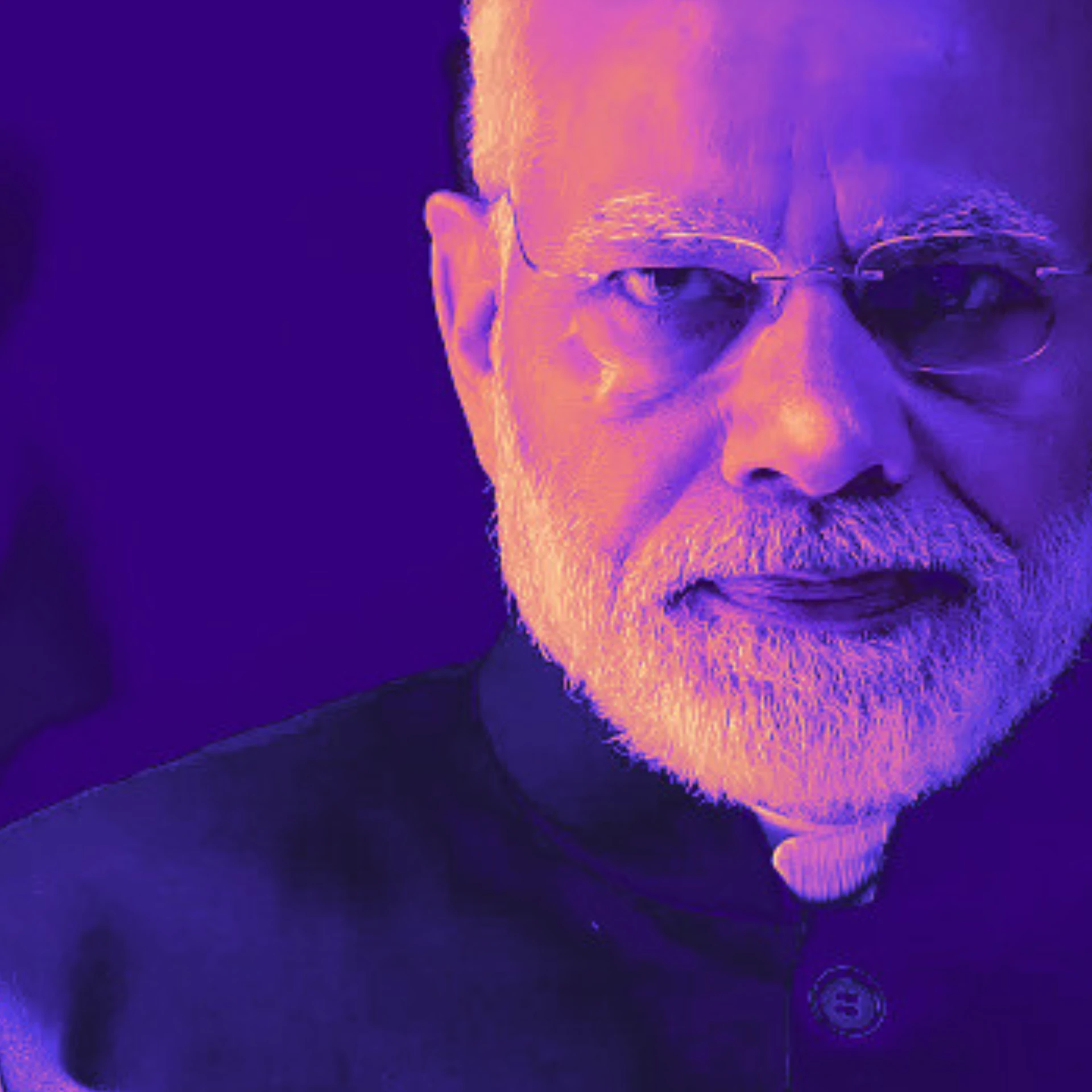 Duotone portrait of a bearded Indian man wearing spectacles, tinted deep purple and orange